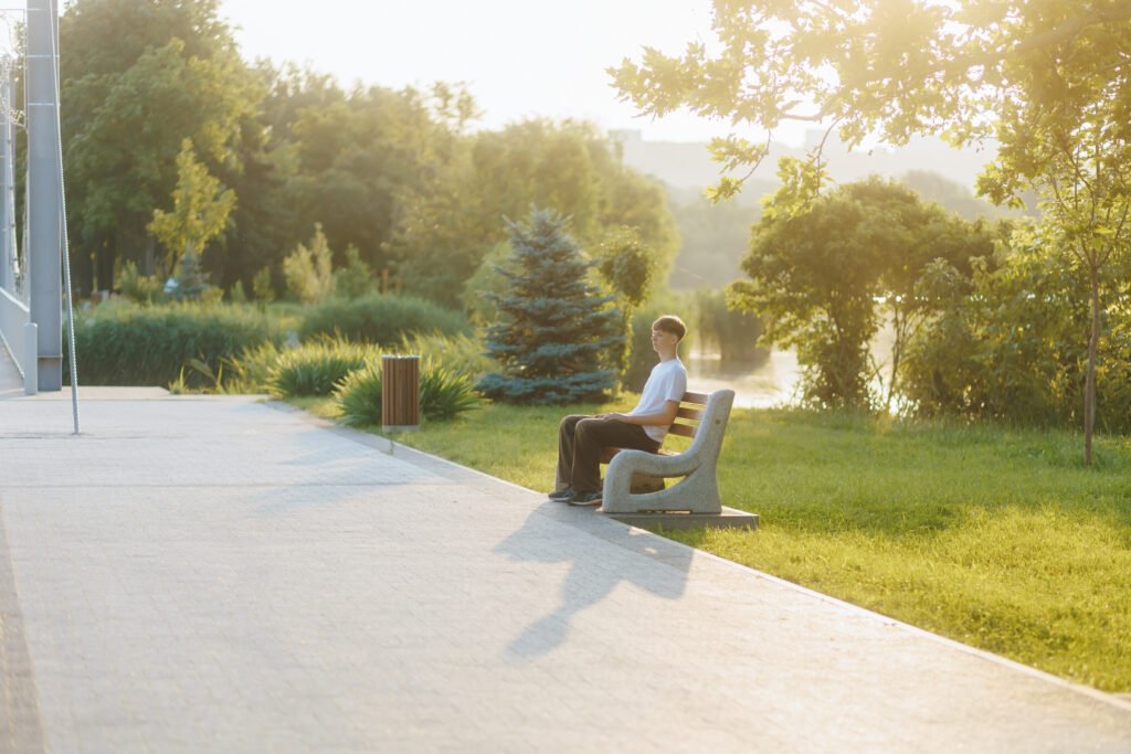 Teen boy sitting alone on park bench in golden hour sunlight