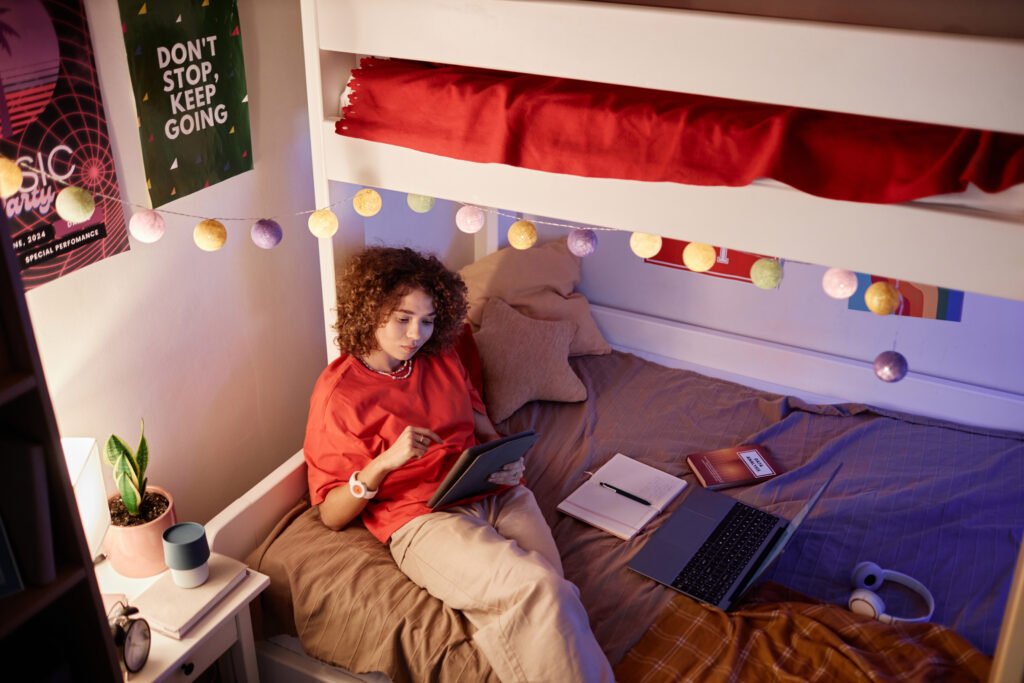 Young Girl Using Tablet Doing Homework on Bunk Bed in College Dorm