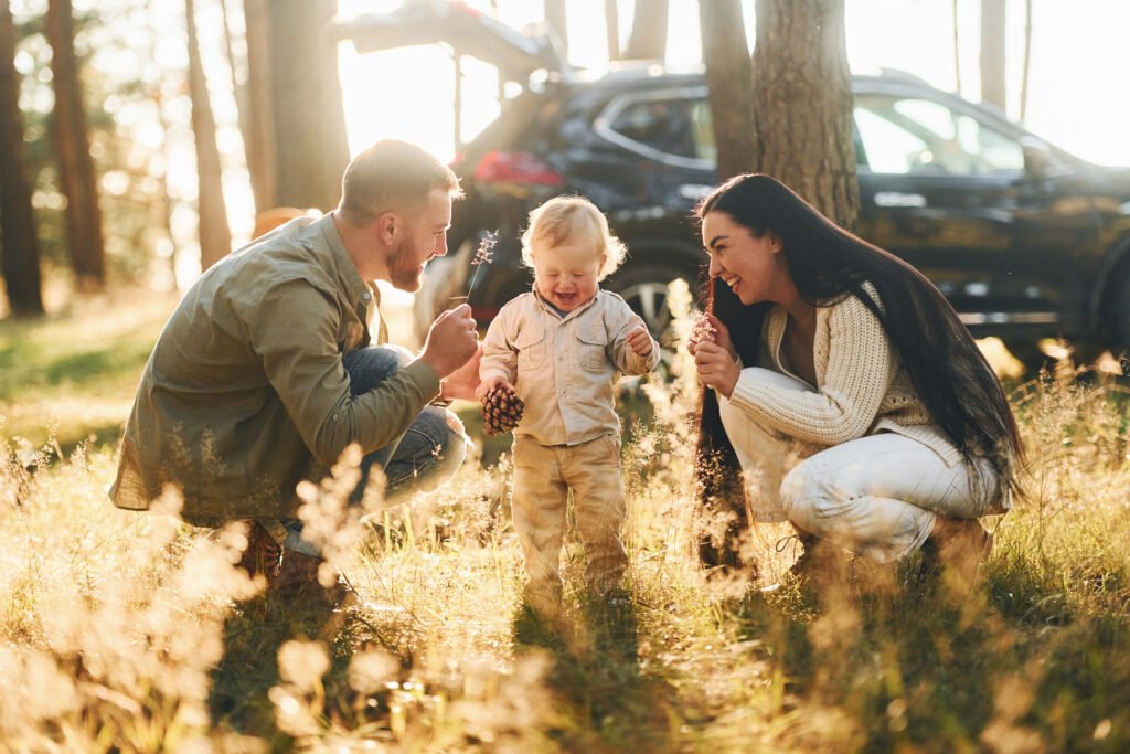 Sitting on the ground. Happy family of father, mother and little daughter is in the forest