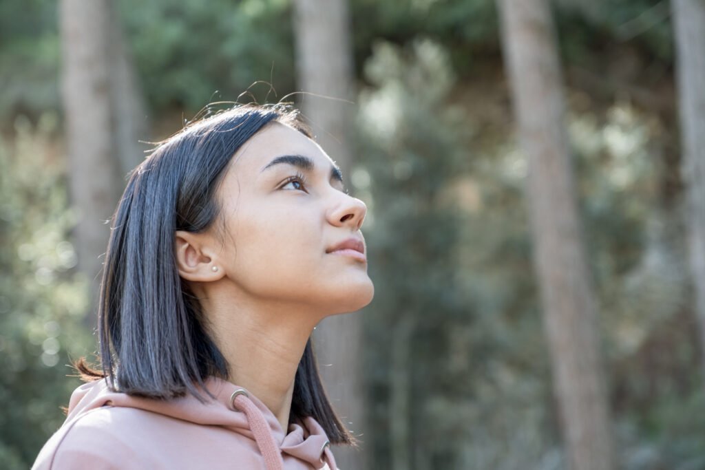 Girl looking at the sky in the middle of the forest in winter with short hair and pale pink sweatshirt.