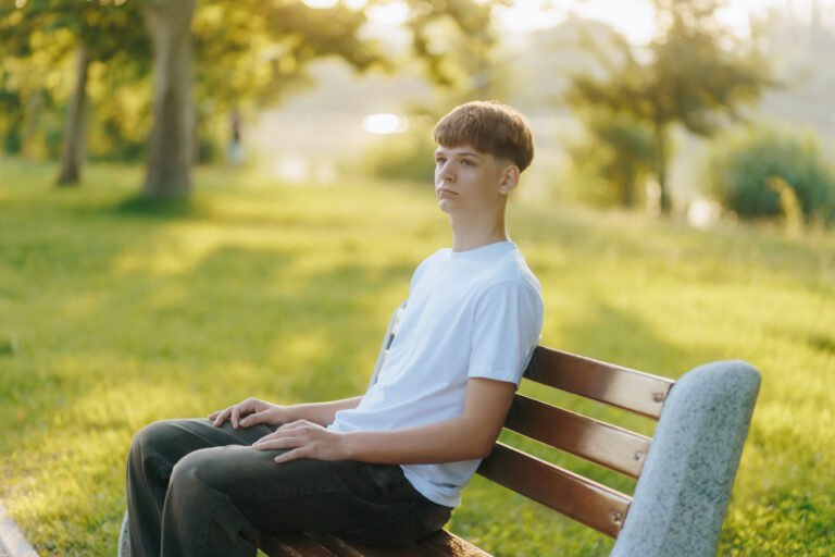 Teen guy in white tee chilling solo on stone bench in green city park