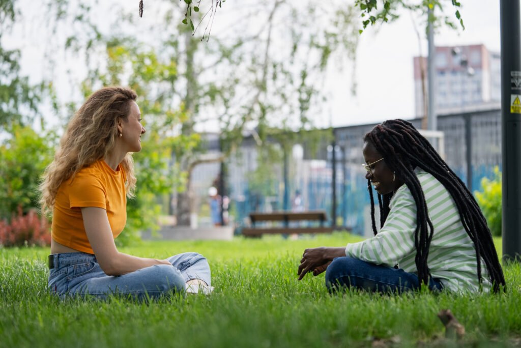 Two young women having a conversation sitting on the grass in a park
