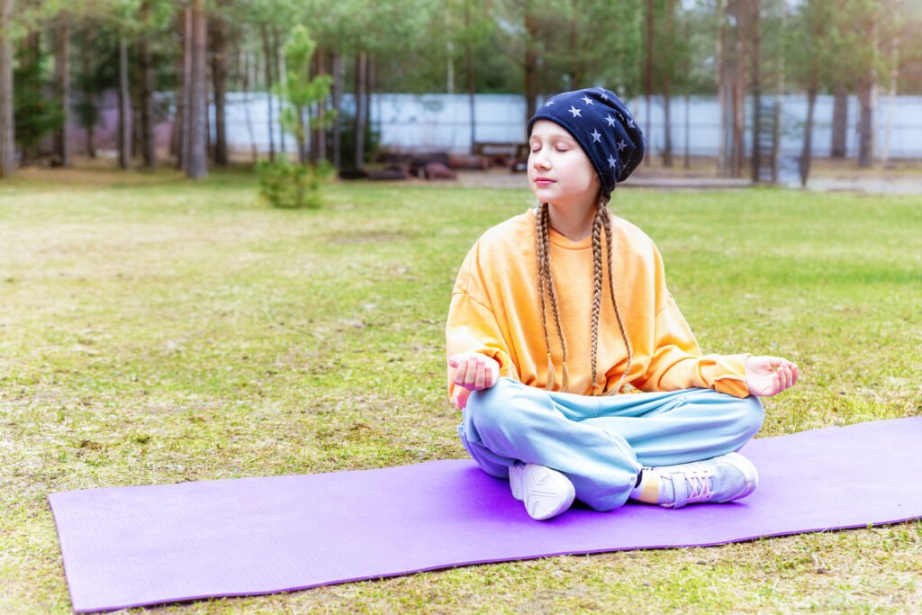 Teenage girl sitting on a sports mat outdoors, meditating with her eyes closed.