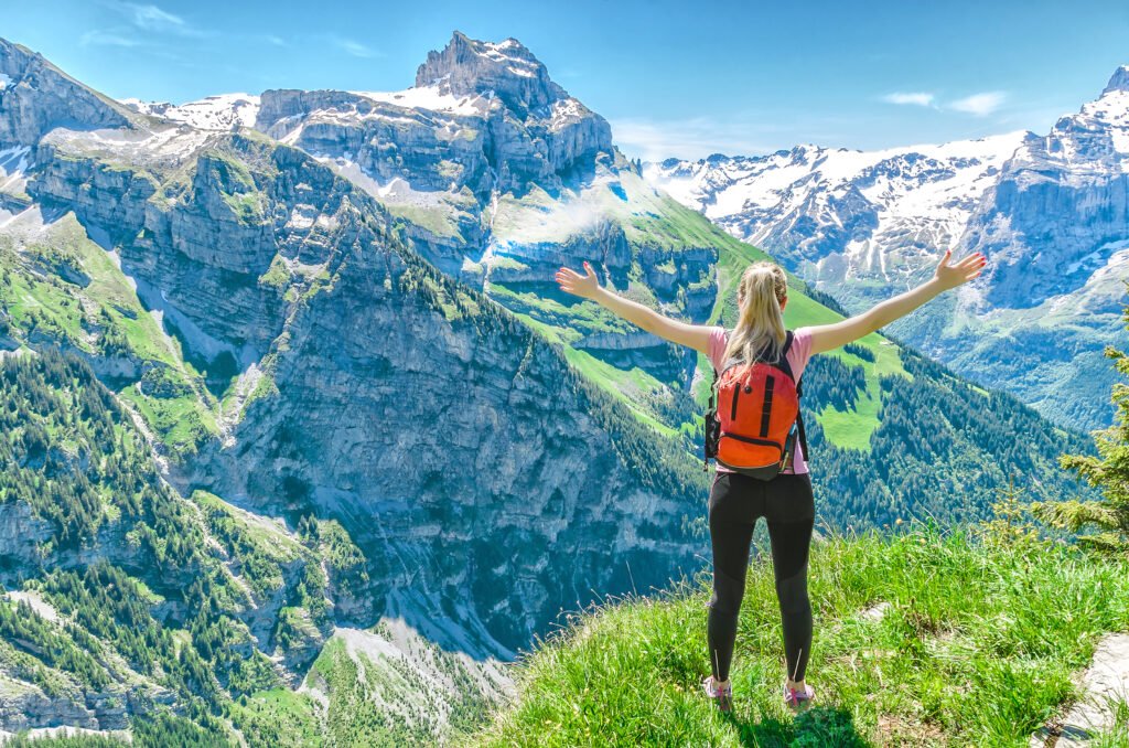 girl traveler, arms outstretched, against the backdrop of mountain peaks