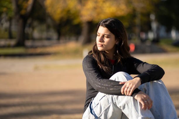 Teenage girl with thoughtful expression sitting in the park