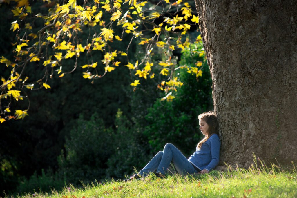 Girl sitting on the grass under maple tree in autumn