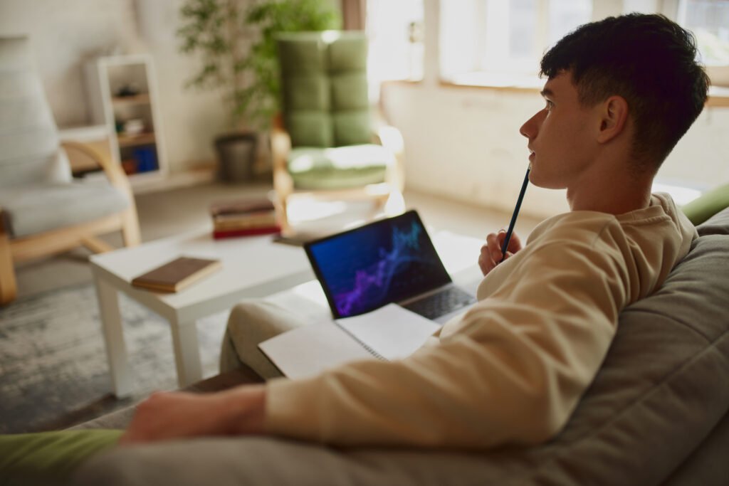 Thoughtful young man, student of economy department sitting at light room at home, laptop with analytical charts. Leaning trading