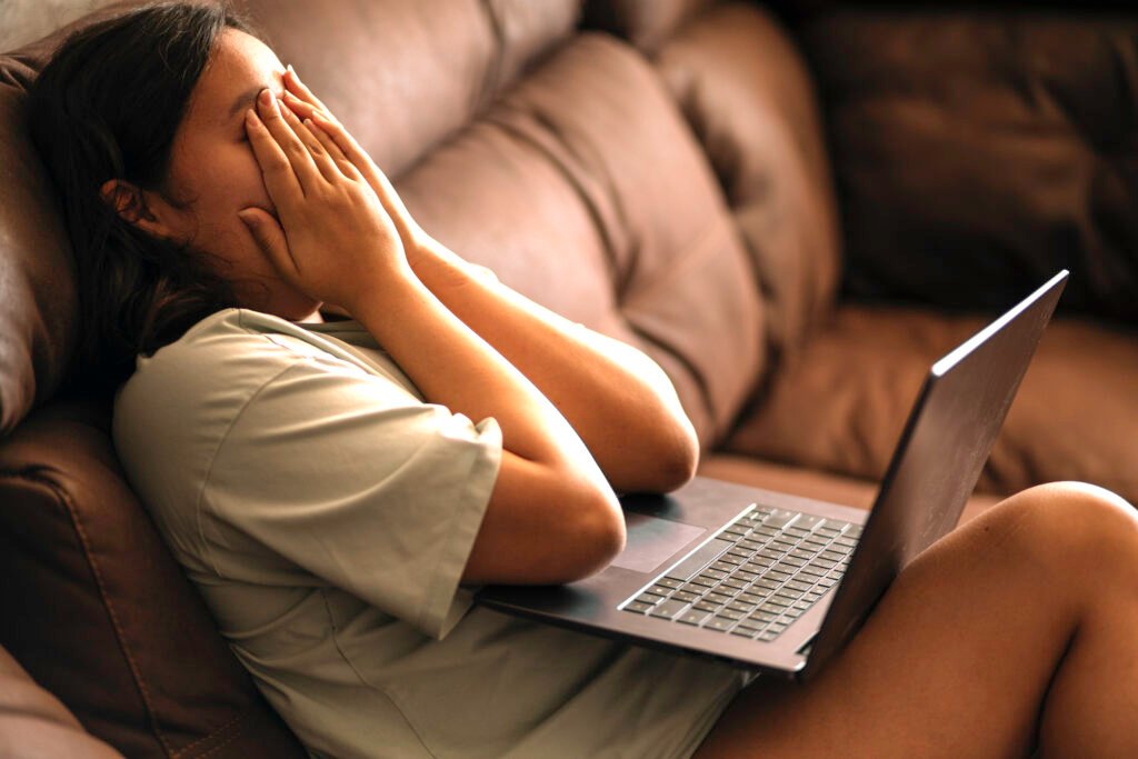 Chubby asian teen girl at home, sitting on the sofa with a laptop on her lap. sad news