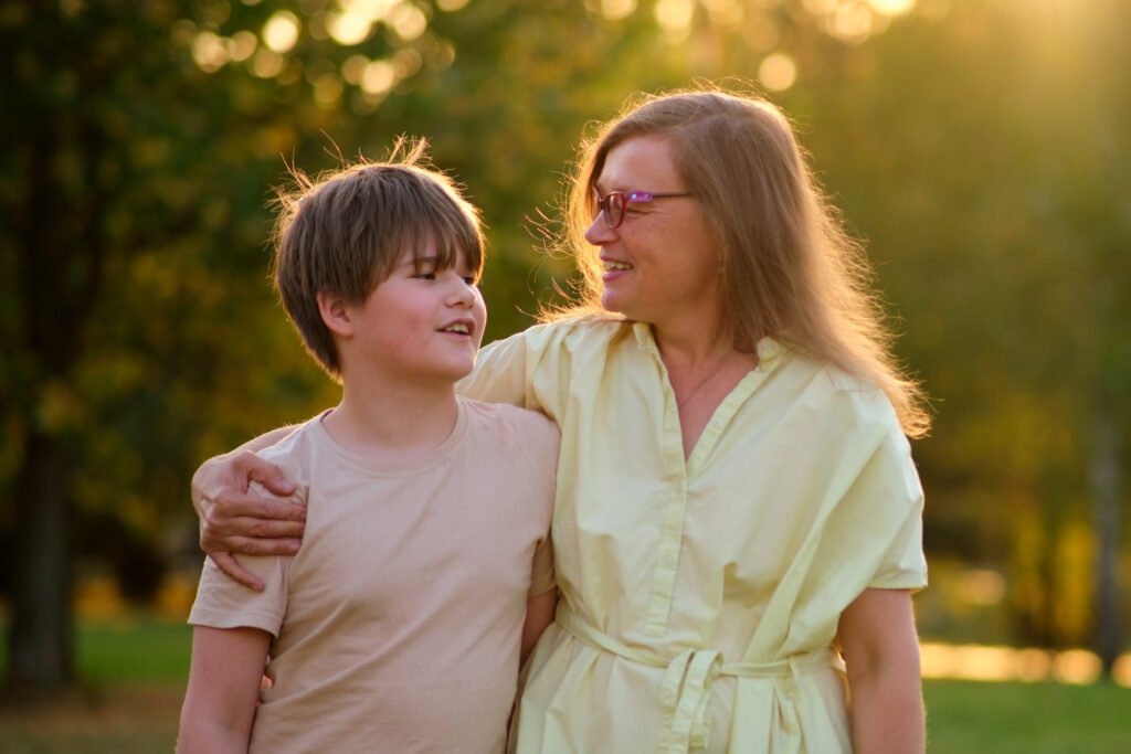 The close relationship between the mother and her boy is evident as they laugh together under the sun. The joy of motherhood shines in the eyes of this woman as she embraces her teenage son in park.