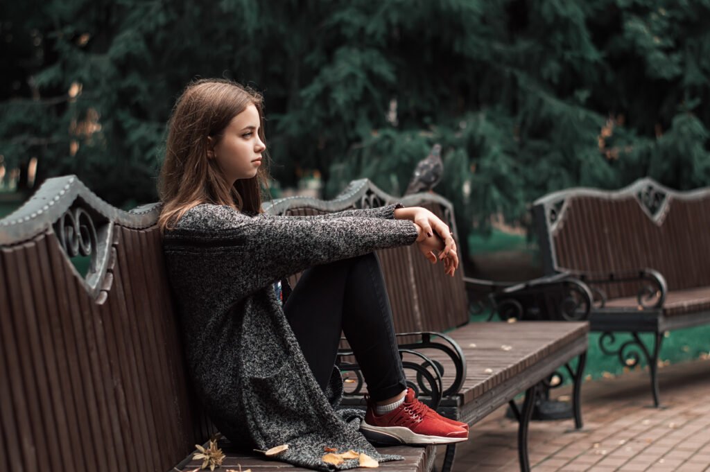 Teenage girl sitting on the wooden bench in the park