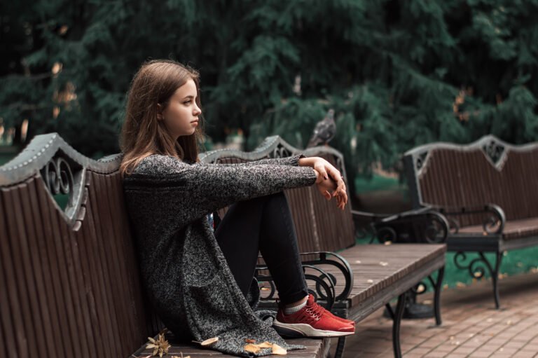 Teenage girl sitting on the wooden bench in the park