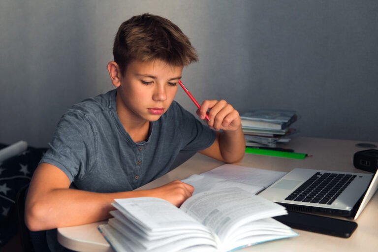 student boy at workplace at home with open copybook and computer