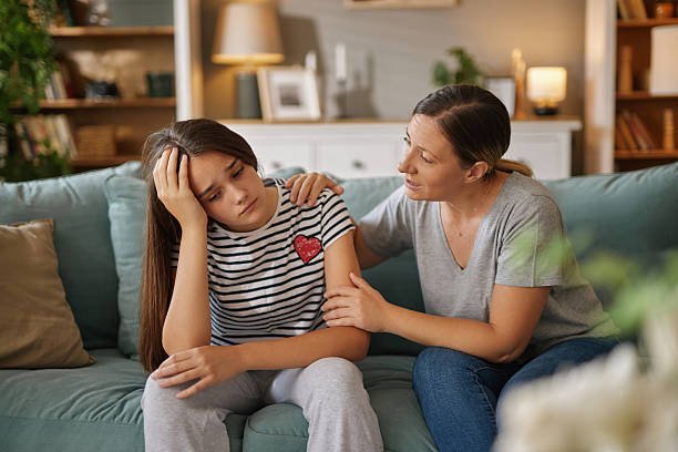 Sad teenage girl sitting on the sofa at home and talking with her mother