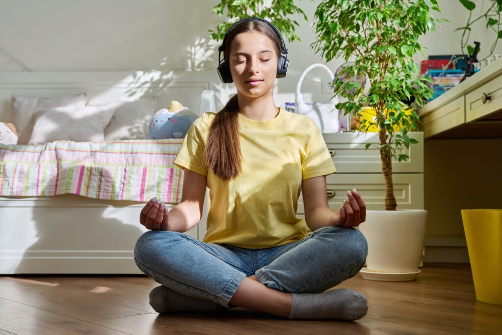 Teenage girl in headphones relaxing with closed eyes sitting in lotus position at home