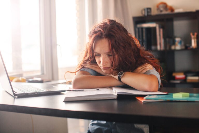 Sad and tired student girl looking on laptop and notebook