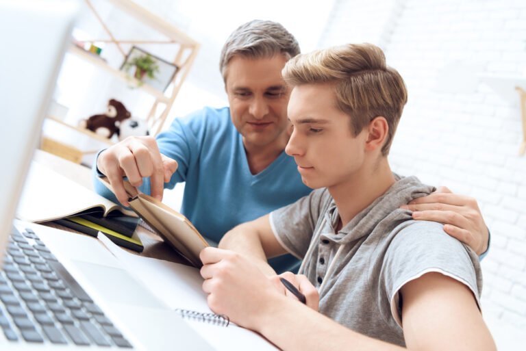 Father helps his son who is doing homework. Troubled teenager tries to study.