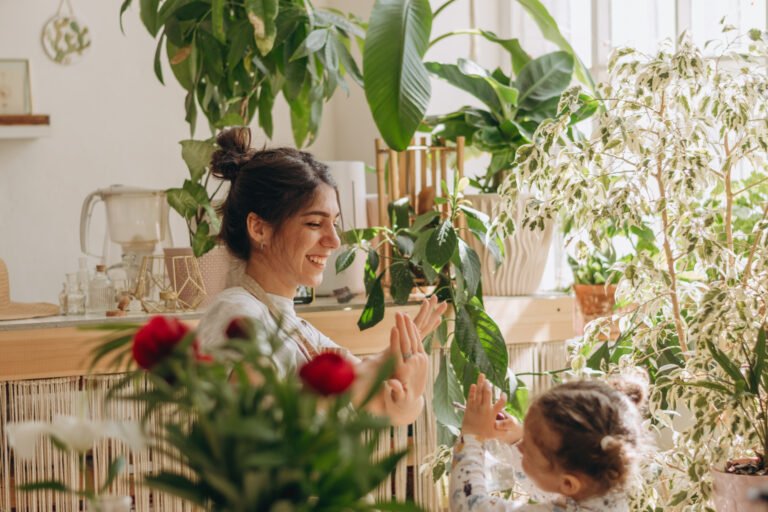 Mixed race family woman with her little daughter is watering houseplants at home and having fun splashing water.Home gardening.Family leisure,hobby concept.Biophilia design and urban jungle concept