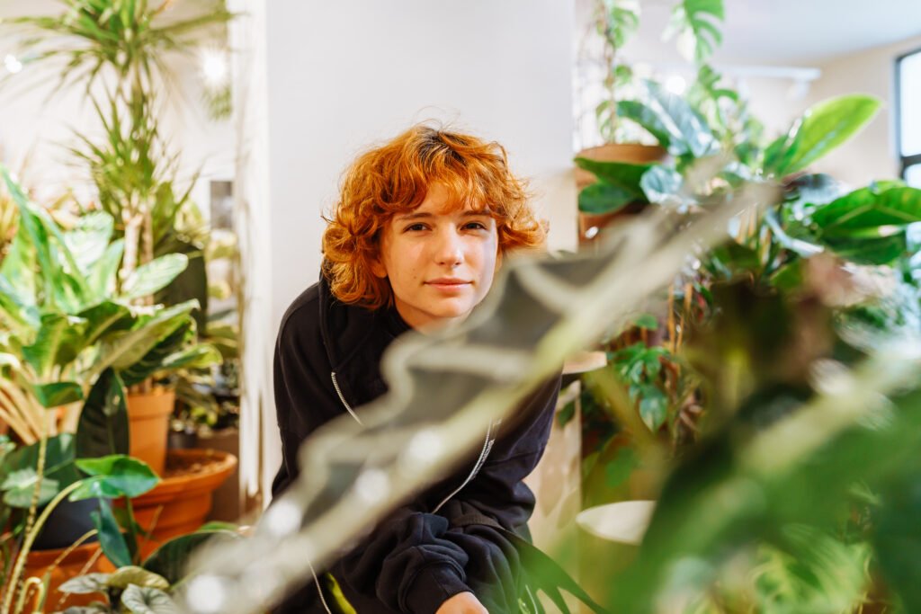 Portrait teenage girl with red-haired curly hair in flower greenhouse