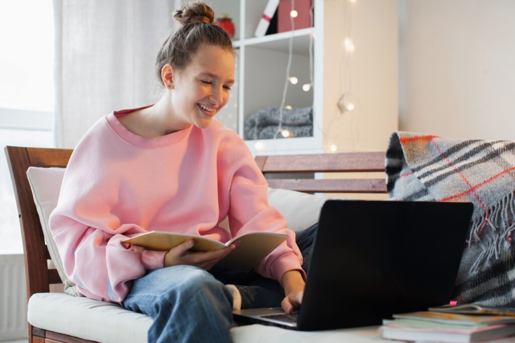 Millennial teen girl sit at couch in living room study on laptop making notes