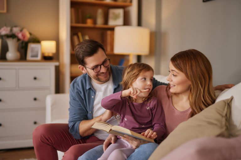 Family with little daughter reading book on sofa in living room
