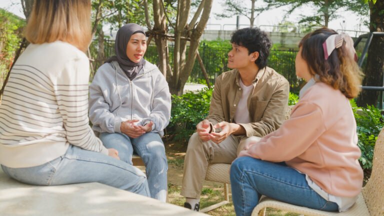 Small Asian group of people sit in a close circle and talk to a therapist in park. Smile people sharing story happy speak diverse people sitting in circle at group therapy session psychologist.
