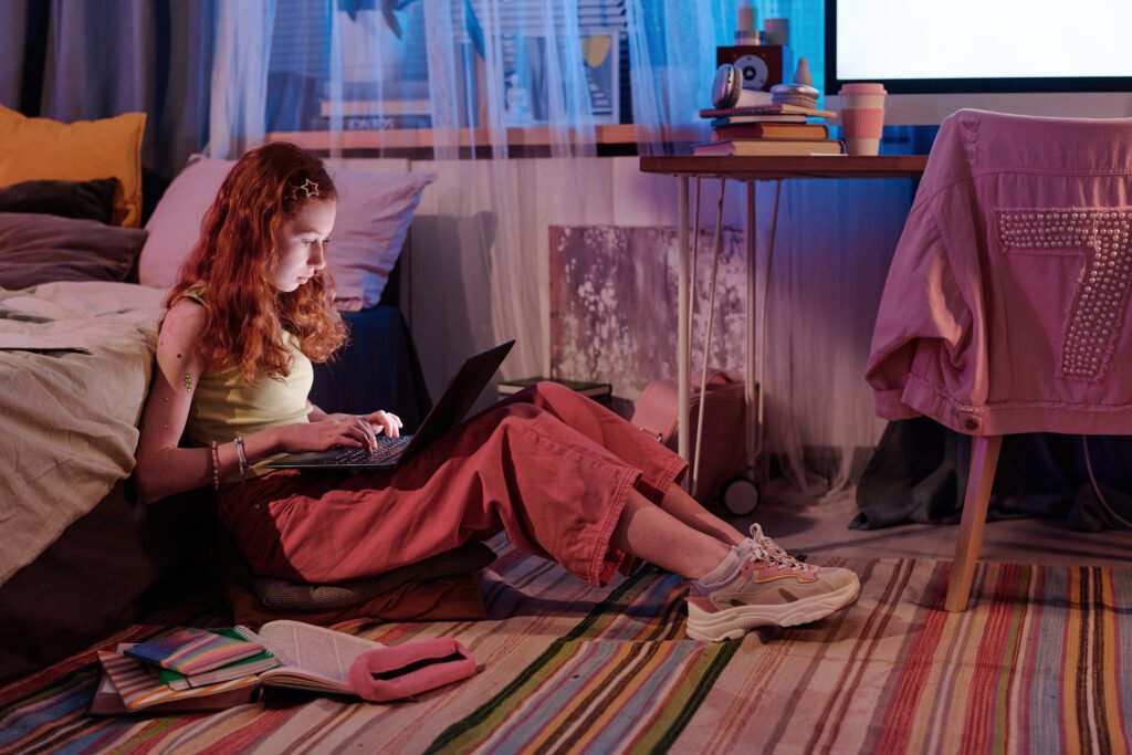 Teenager Sitting On Floor In Bedroom Using Laptop