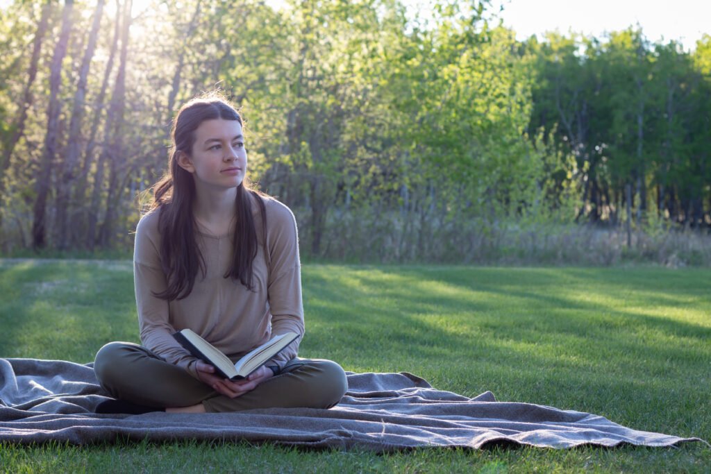 Teenage girl reading on blanket outside