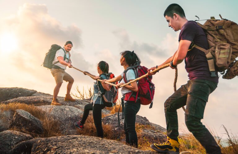 Young asian four hikers climbing up on the peak of mountain. People helping each other hike up a mountain at sunlight. Giving a helping hand. Climbing. Helps and team work concept