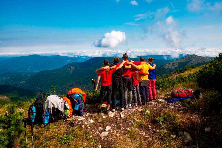 Hikers, friends stand, embracing on a mountain top
