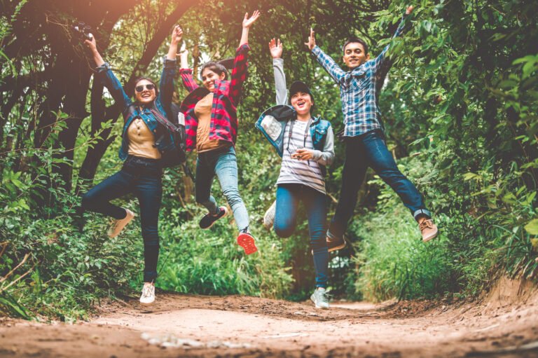 Group of happy Asian teenage adventure traveler trekkers group jumping together in mountain at outdoor forest background. Young hiker friends supporting each others as survival team travel and success