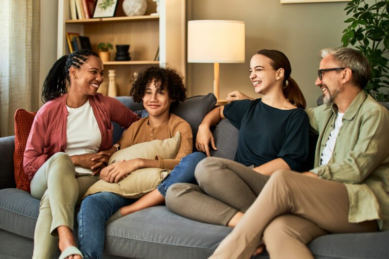 A happy family of different races and ages sitting together on a couch and talking.