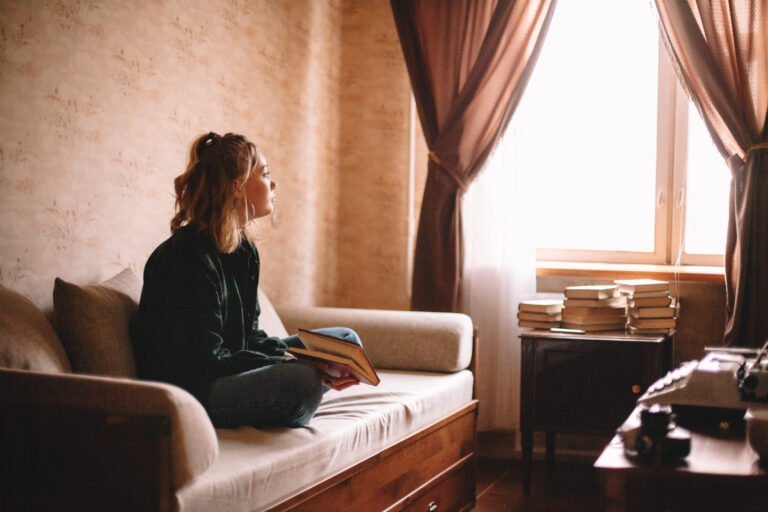 Young woman holding book while sitting on sofa at home