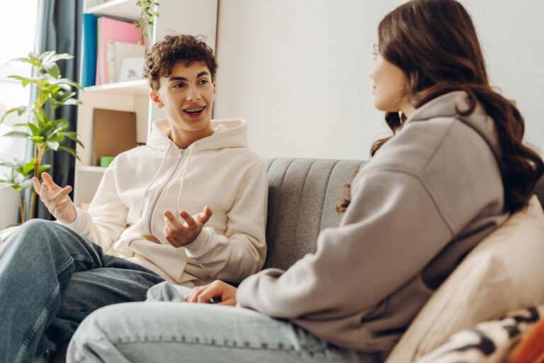 Teenagers talking, sitting together on sofa at home in living room