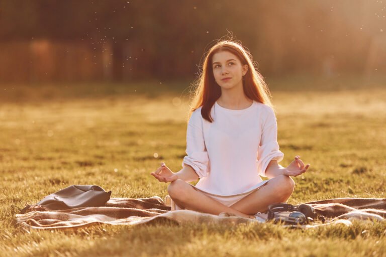 Doing yoga on the mat. Young girl is on the field at sunny daytime having nice weekend