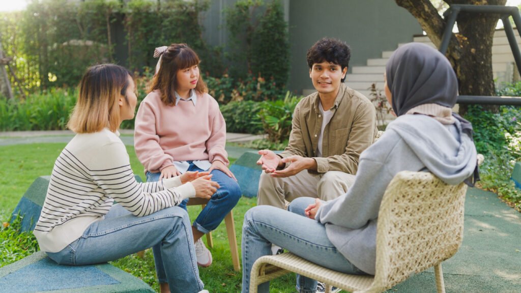 Small Asian group of people sit in a close circle and talk to a therapist in park. Smile people sharing story happy speak diverse people sitting in circle at group therapy session psychologist.