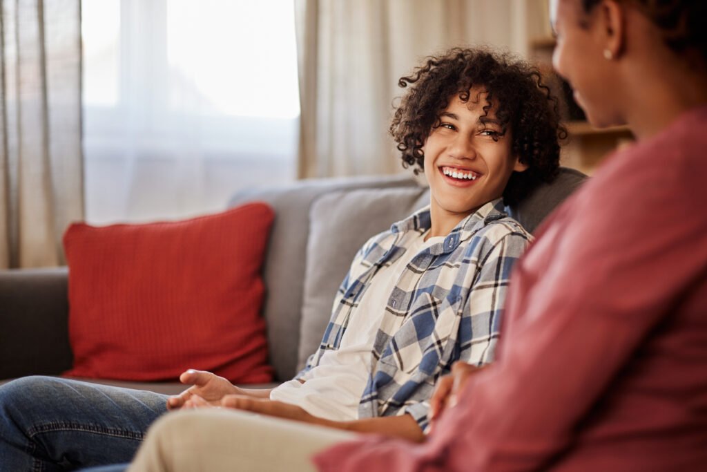 A smiling African-American teenage boy in a plaid shirt and jeans talking with his mother.
