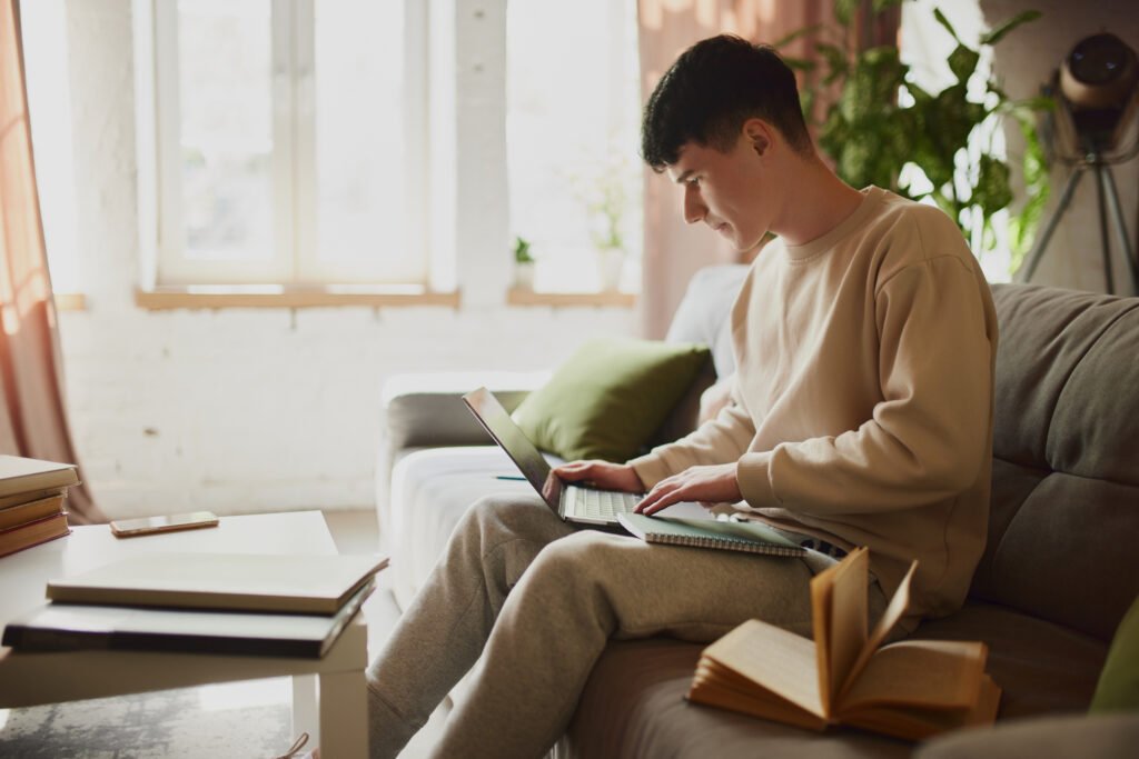 Teenage boy, student sitting on couch at home and looking on laptop with concentration and focus. High level of productivity