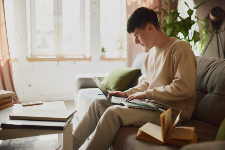 Teenage boy, student sitting on couch at home and looking on laptop with concentration and focus. High level of productivity