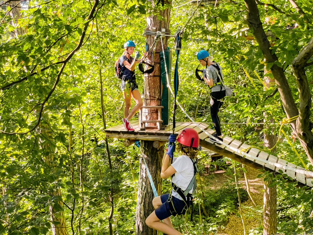 A people walks a rope bridge between trees in an amusement park in safety gear and a helmet. Adventure park close-up. Summer fun and sports for adventurous people. Rope park in wood forest.High-altitude climbing training on adventure track