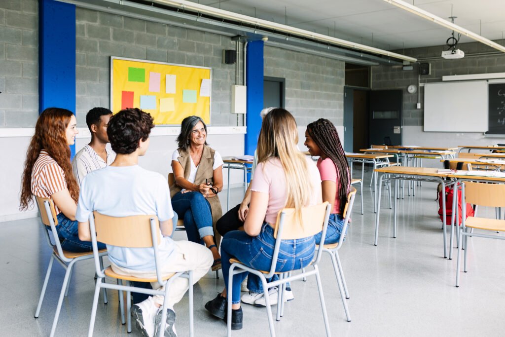 Young group of teenage students discussing in classroom with teacher