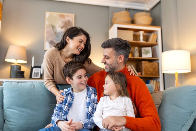 Happy family having fun at home, parents and little children sit on sofa together, Happy family sitting on sofa laughing together. Cheerful parents playing with their kids at home.