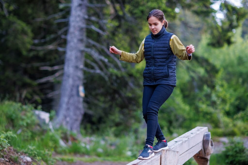Teenage girl walks along an inclined log and passes a forest obstacle course in a pine forest
