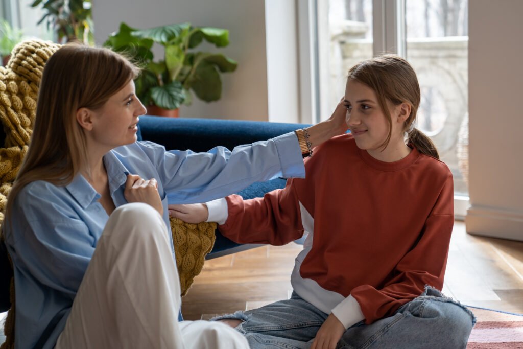 Young happy mother and teen daughter talking while sitting on floor