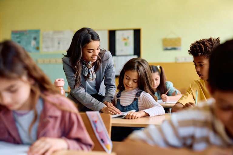Happy Hispanic teacher assisting schoolgirl during a class at elementary school.