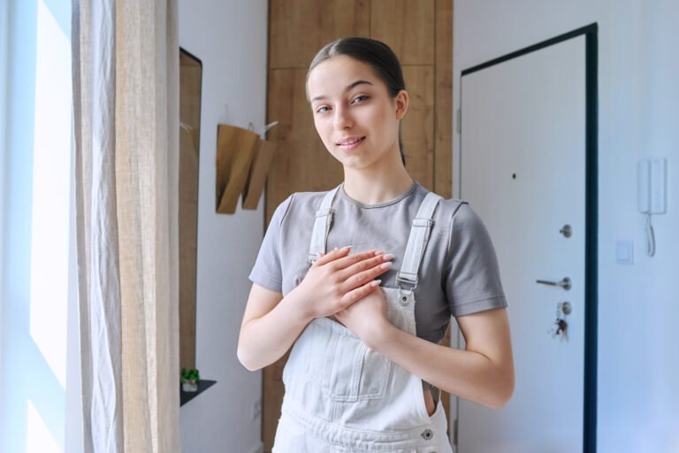 Calm smiling teenage girl holding hands on chest over heart