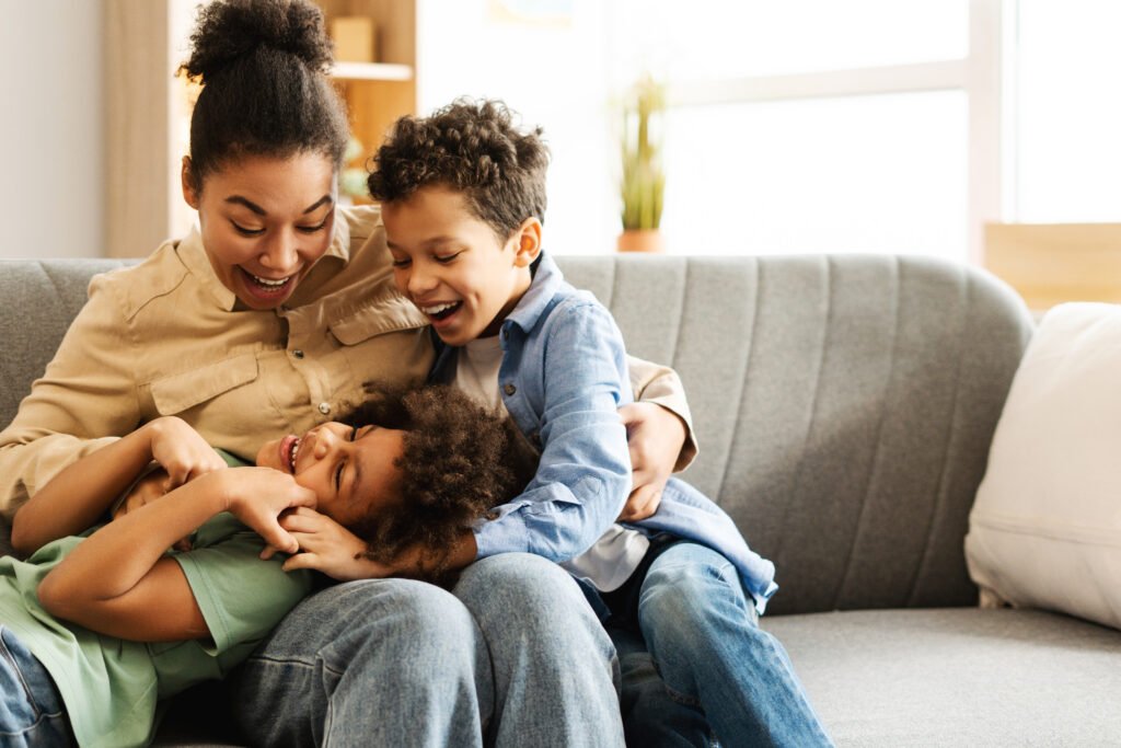 Cute boy and girl with their mother fooling around together, sitting on comfortable sofa at home
