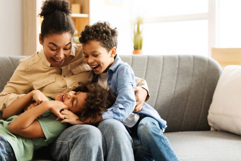 Cute boy and girl with their mother fooling around together, sitting on comfortable sofa at home