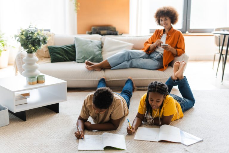 Smiling mother sitting on sofa, little daughter and son lying on floor drawing