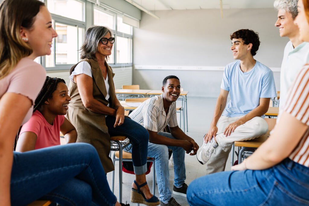 Young group of high school students talking with mature teacher in classroom