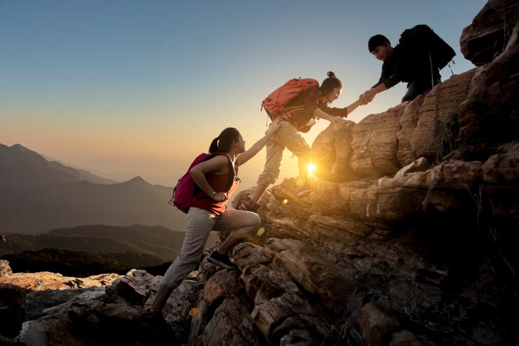 Group of Asia hiking help each other silhouette in mountains with sunlight.